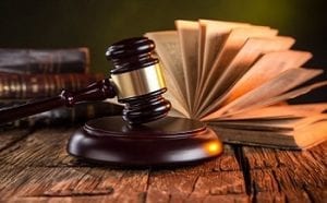 A wooden gavel and block rest on a desk with books in the background. 