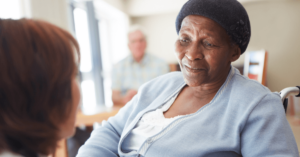 An older adult in a wheelchair listens intently to a caregiver in a nursing home.