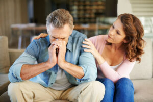 A distressed person on a couch being comforted by someone beside them with a hand on their shoulder.