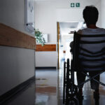 A nursing home resident in a wheelchair sits in an empty hallway.