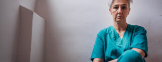 A woman in green scrubs sits against the wall, appearing to be exhausted.