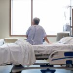 A man in a hospital bed or nursing home faces away at the wall.