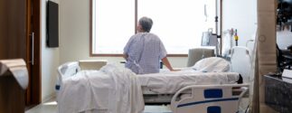 A man in a hospital bed or nursing home faces away at the wall.