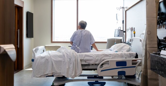 A man in a hospital bed or nursing home faces away at the wall.