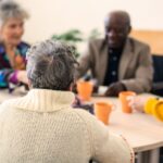 A group of different types of senior citizens sit at a table while appearing to be social.