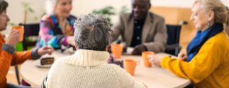 A group of different types of senior citizens sit at a table while appearing to be social.