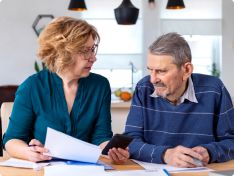 An ombudsman for nursing homes explains paperwork to her client at a desk.