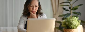 A woman sitting at a table, looking thoughtfully at her laptop screen.